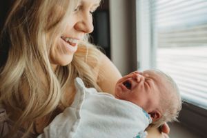 A precious moment with a crying newborn being comforted in a cozy room by window light.