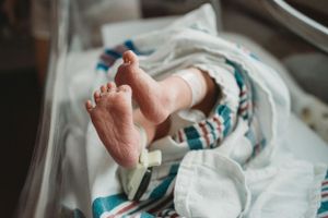 Tiny newborn baby foot resting on hospital bedding with medical equipment nearby.
