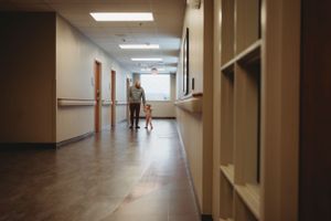 Distant view of people walking down a long hospital hallway with fluorescent lighting.