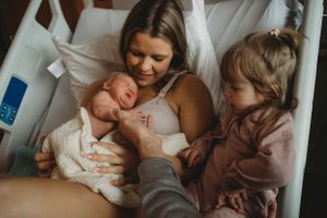 Tender family moment in a hospital bed with a newborn and toddler.
