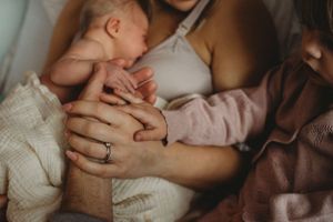 Intimate close-up of gentle hands cradling a sleeping newborn in soft lighting.