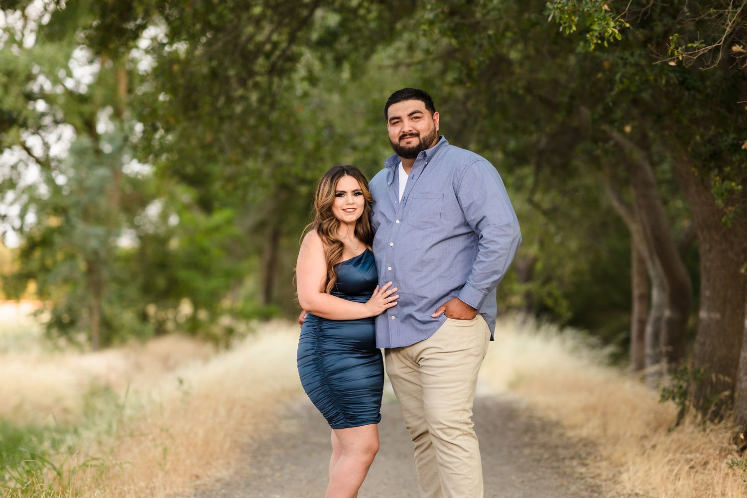 Couple posing together on a tree-lined dirt path during golden hour photoshoot.