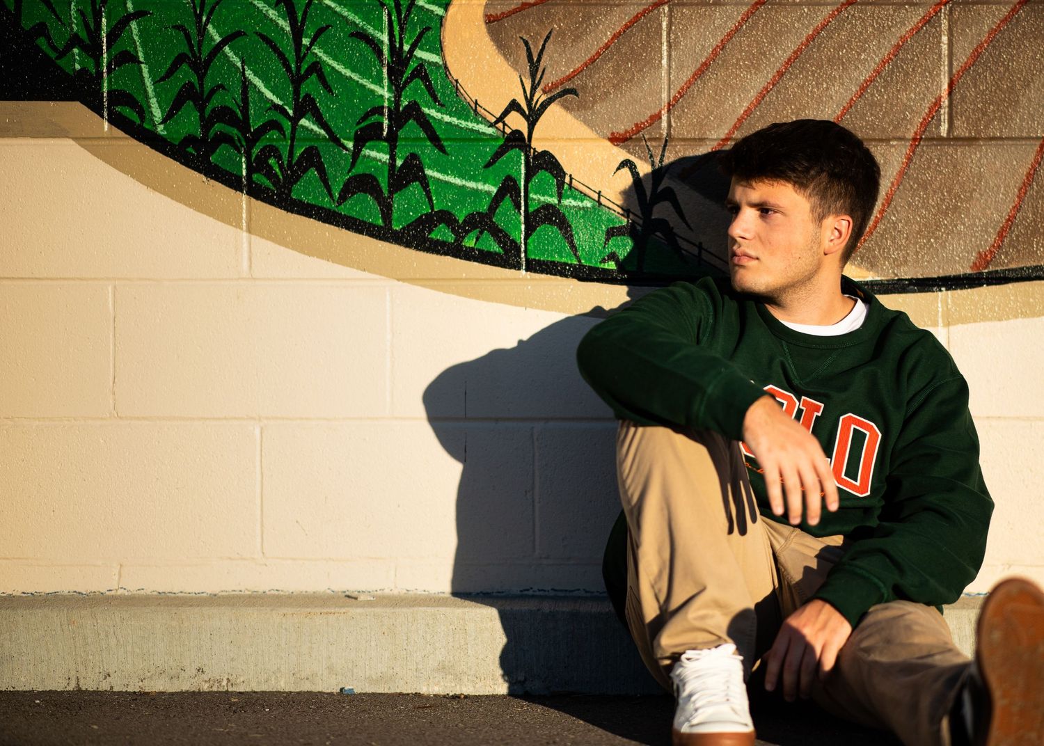 Senior Boy cool and casual with glow of the sunset casting shadow on mural wall.