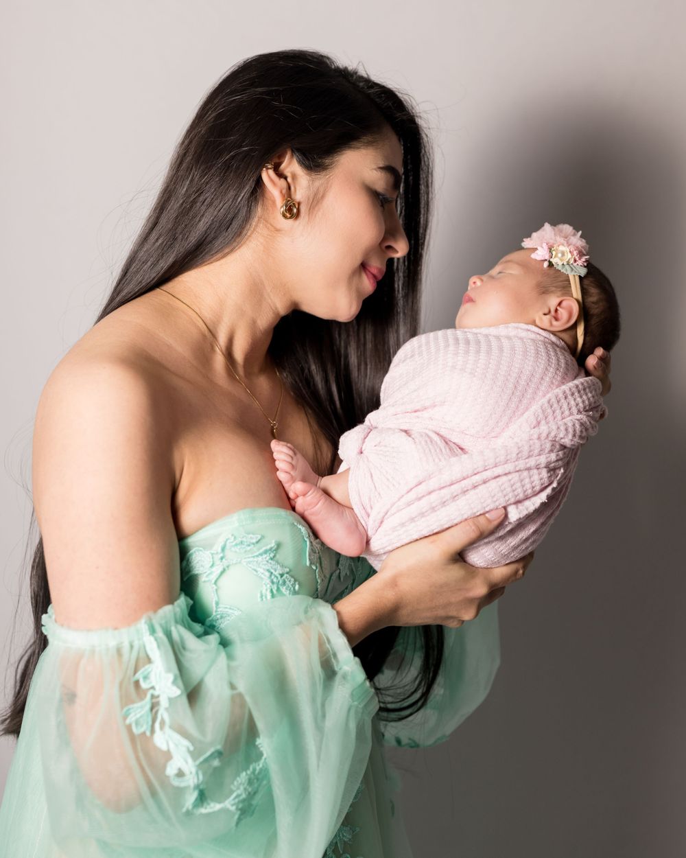 A tender moment between parent and baby against grey background.