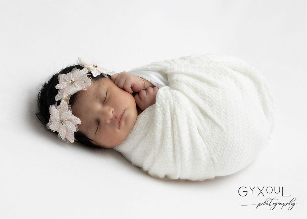 Peaceful sleeping newborn swaddled in white with delicate floral headpiece.