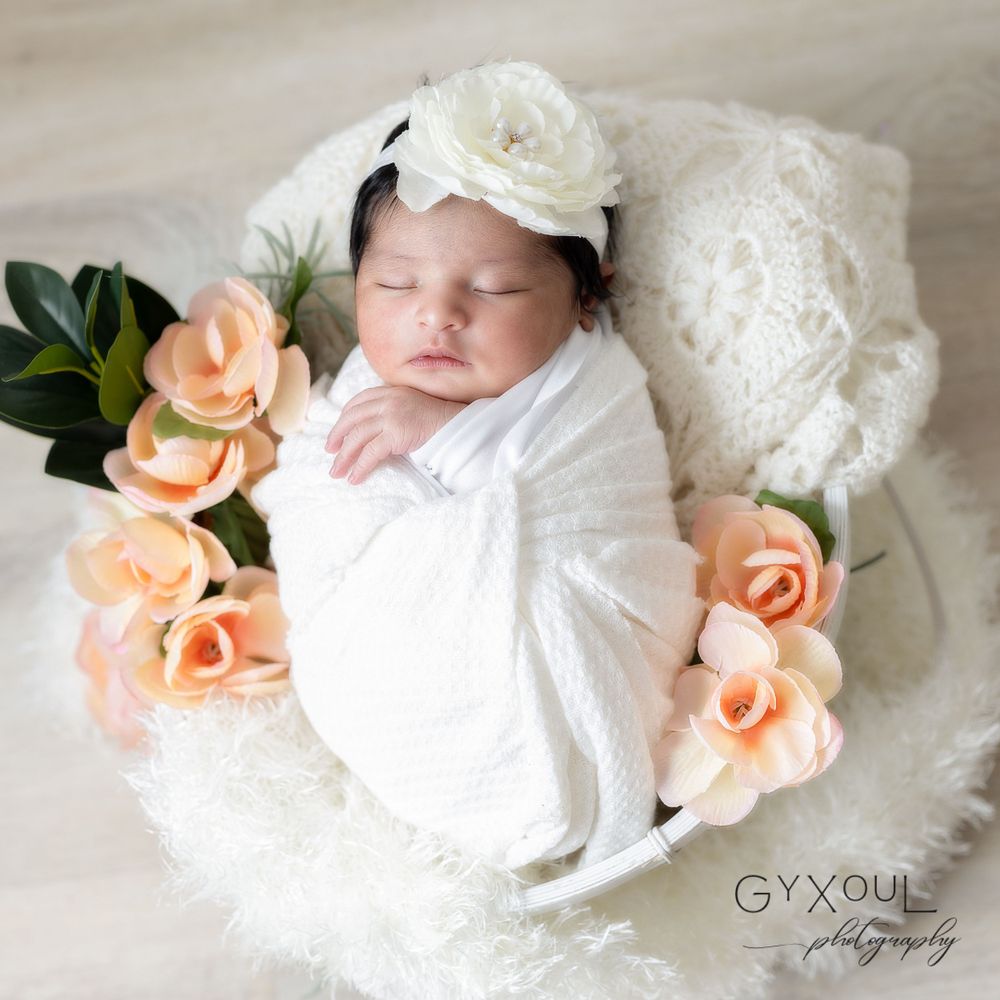 A sleeping newborn wrapped in white with peach roses and a floral headband.