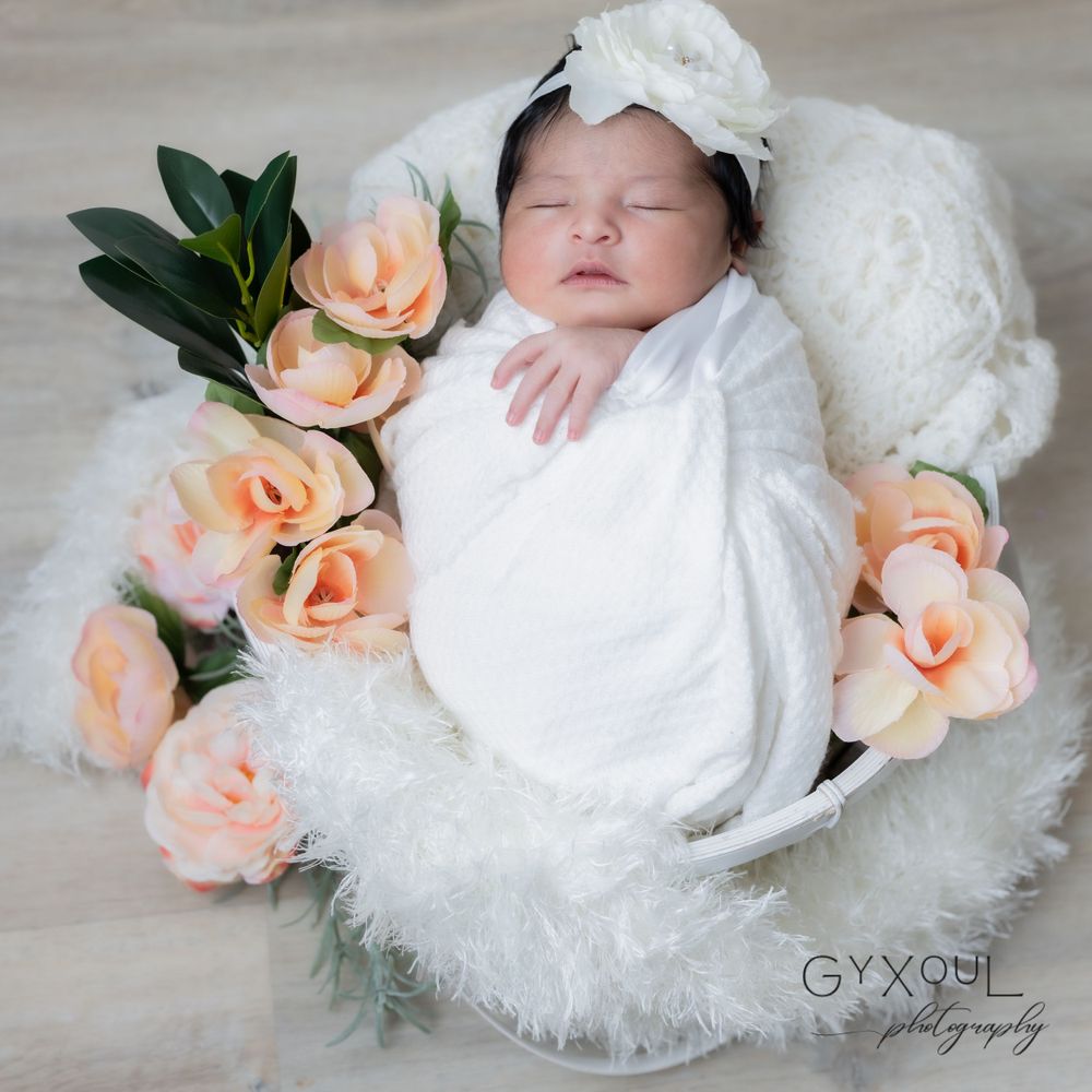 Newborn baby wrapped in white, surrounded by peach roses in a white basket.