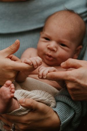Gentle hands caressing a newborn baby wrapped in a knitted blanket.