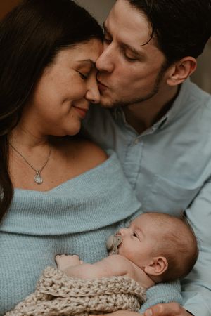 Intimate family moment with a newborn swaddled in a cream knit blanket.