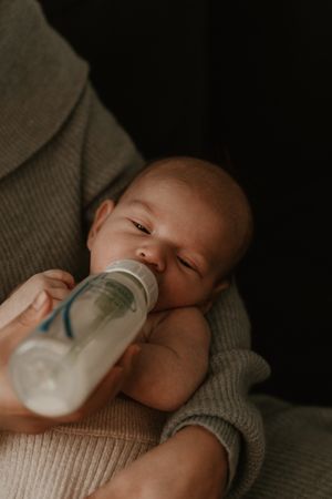 Sleepy newborn drinking from bottle in soft moody lighting.