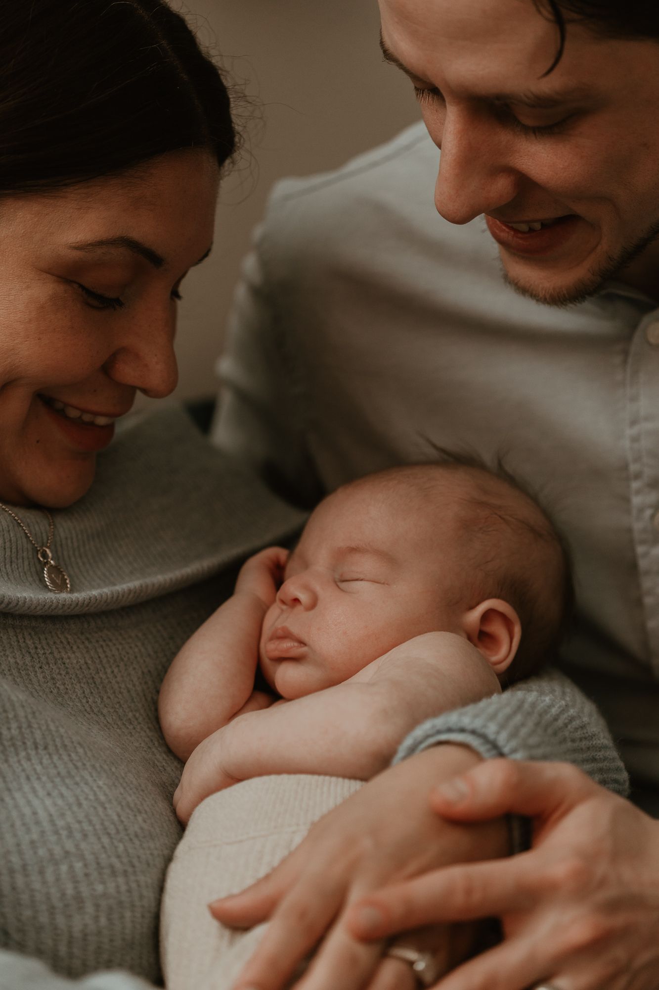 Tender moment with sleeping newborn wrapped in cozy gray sweater.
