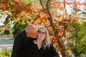 Romantic couple poses outside lovingly under colourful leaves in an autumn setting.