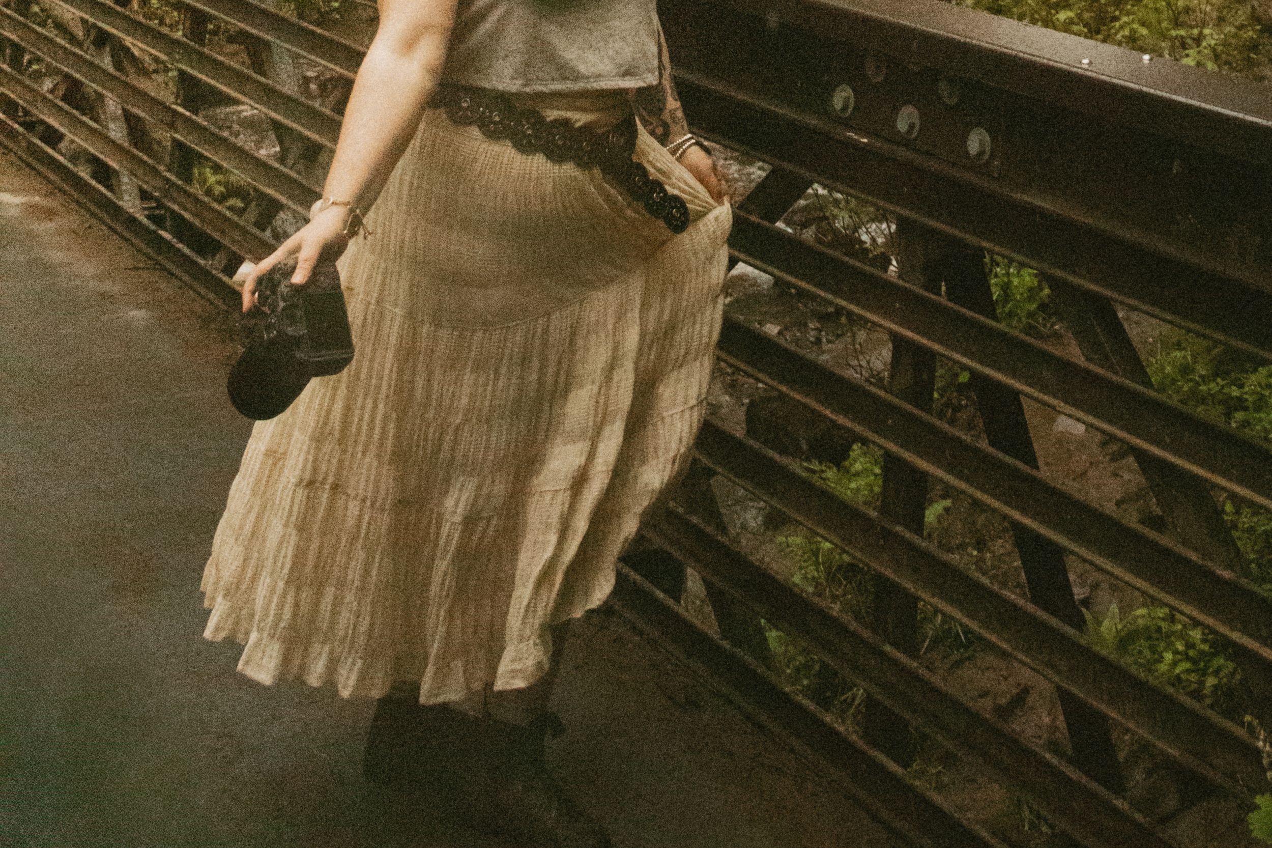 Person wearing brown cardigan and blue jeans writes in spiral notebook while seated at rustic wooden surface.