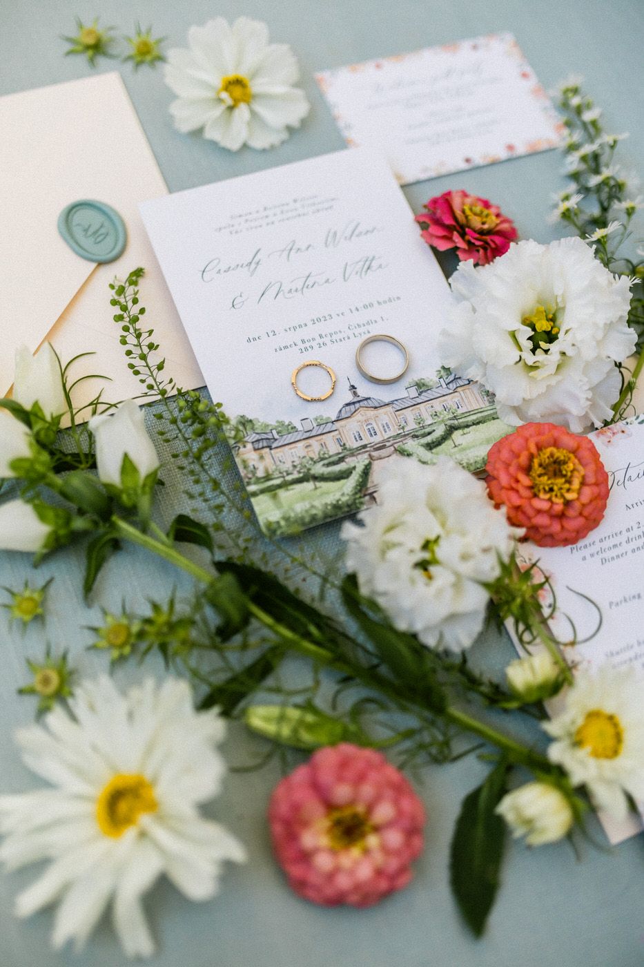 Wedding invitation suite with rings and fresh flowers on light blue background.