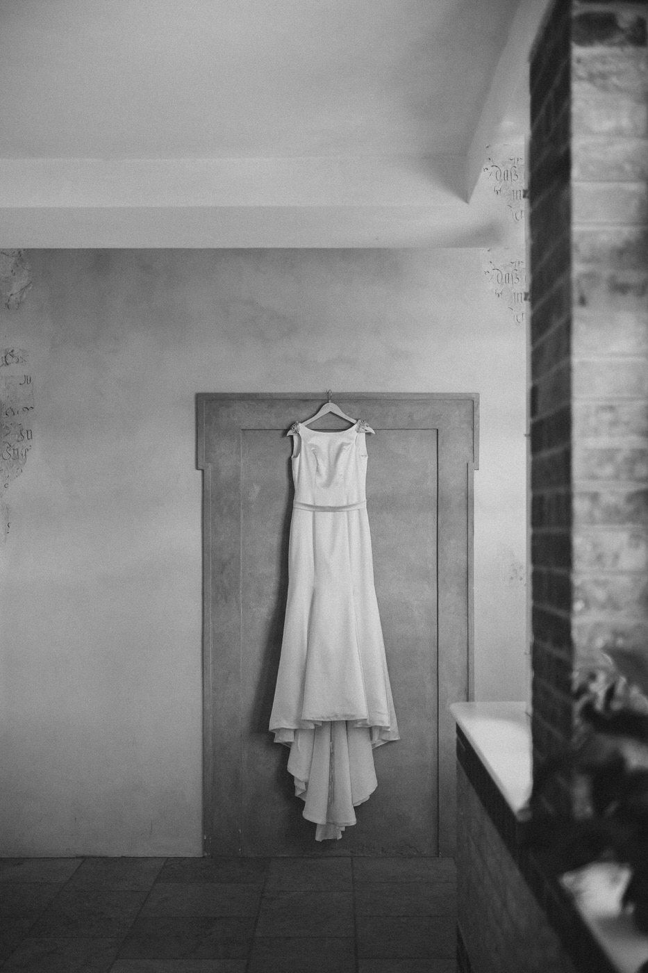 White wedding dress hanging on wooden door in black and white photography.