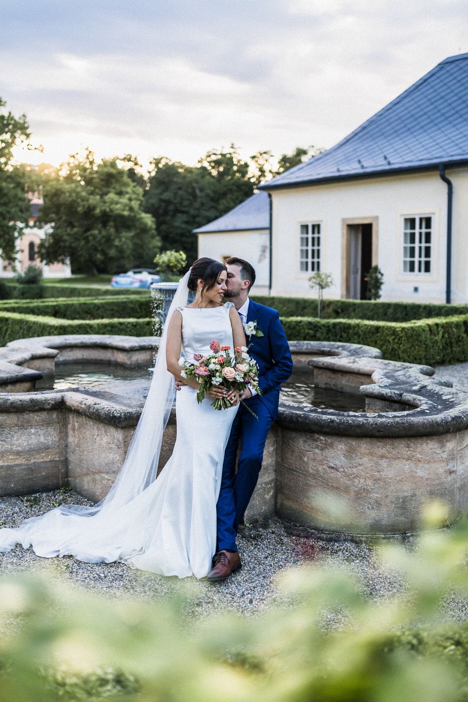 A romantic wedding moment captured near an ornate garden fountain.