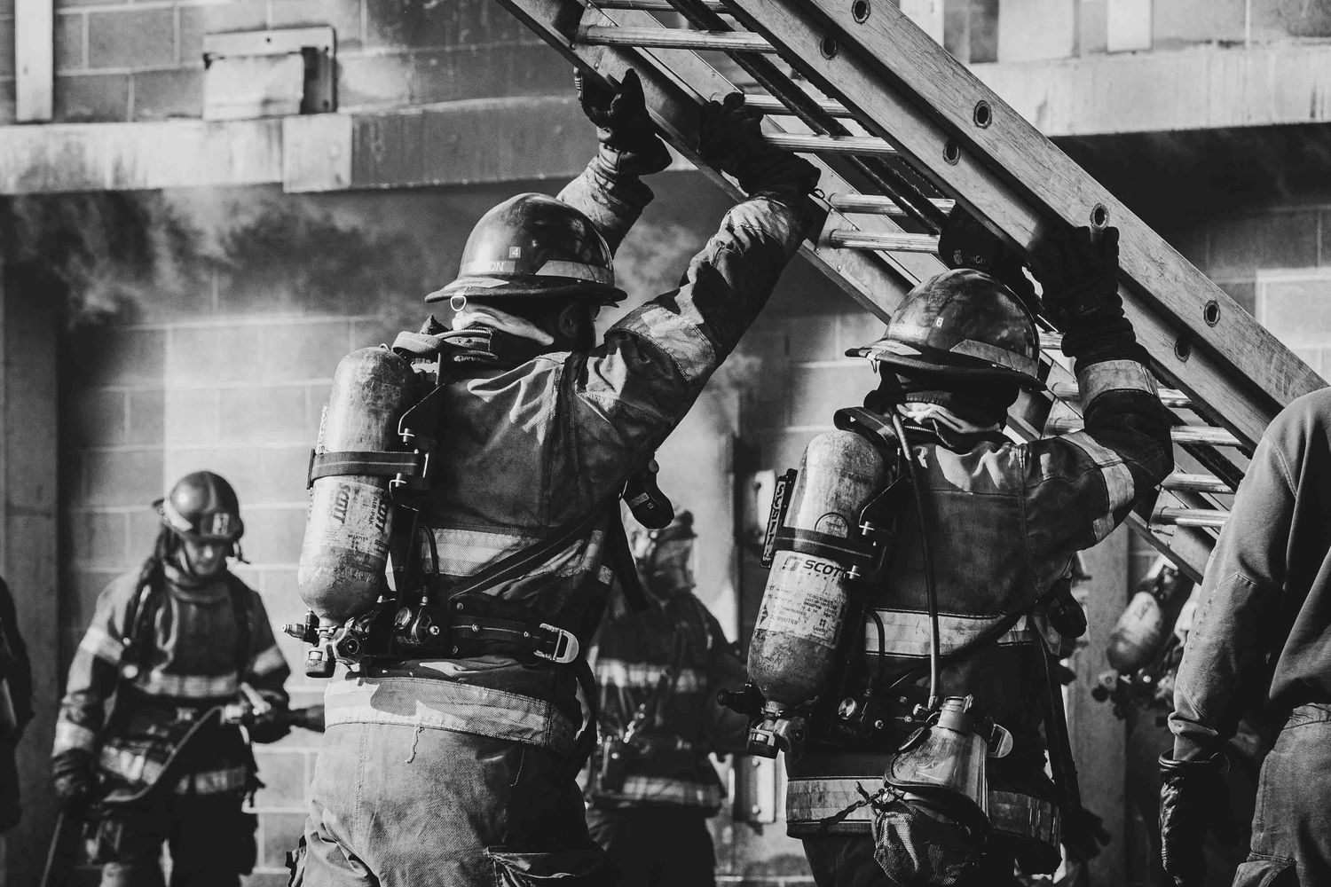 A group of firefighter trainees at the Tri C firefighter academy raising a ladder at a controlled burn for their final exam.