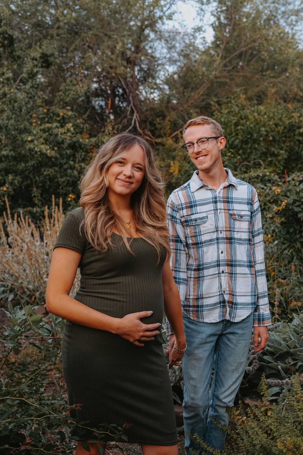 An expectant couple poses together in a garden during fall season.