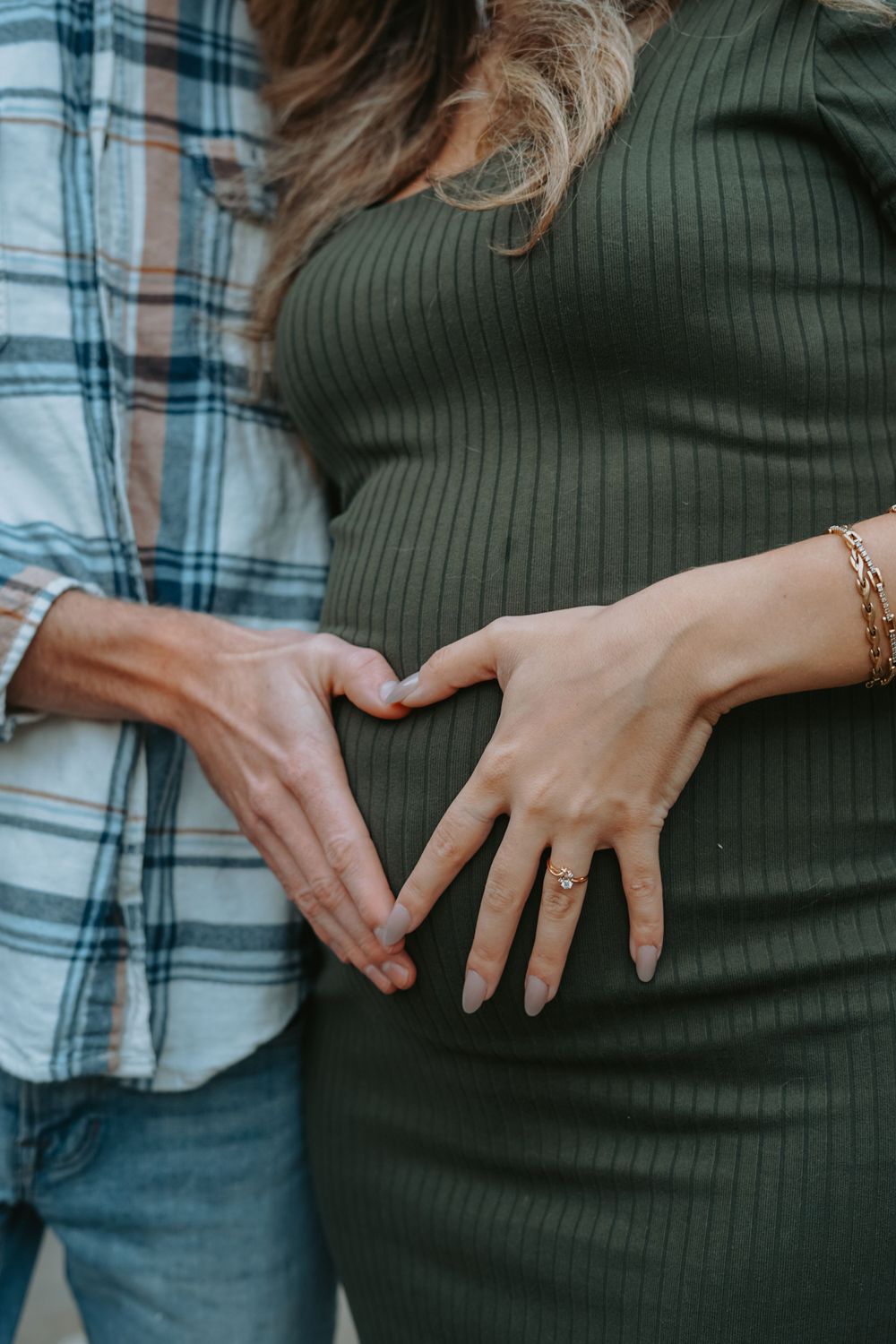 Hands forming a heart shape over a pregnant belly in an intimate maternity photo.
