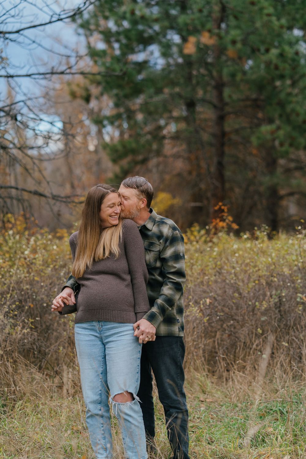 A couple shares tender moments together in a field during autumn, wearing casual clothing and embracing lovingly.