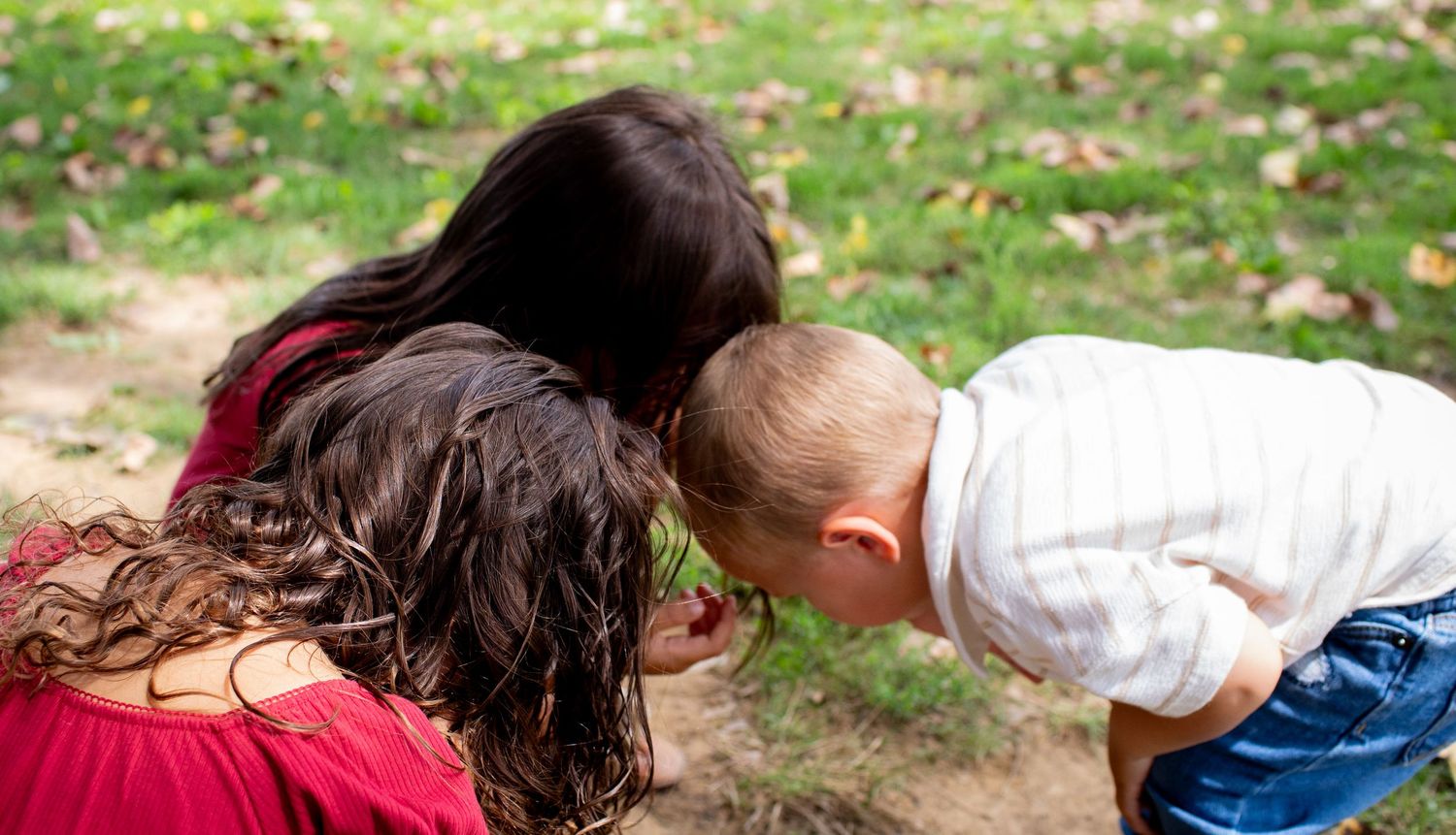 3 kids bend down to examine something interesting on the ground.