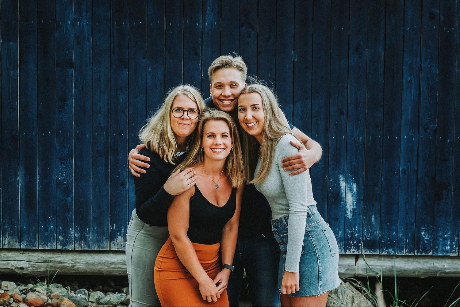 A cheerful group of four friends posing together against a dark blue wooden background.