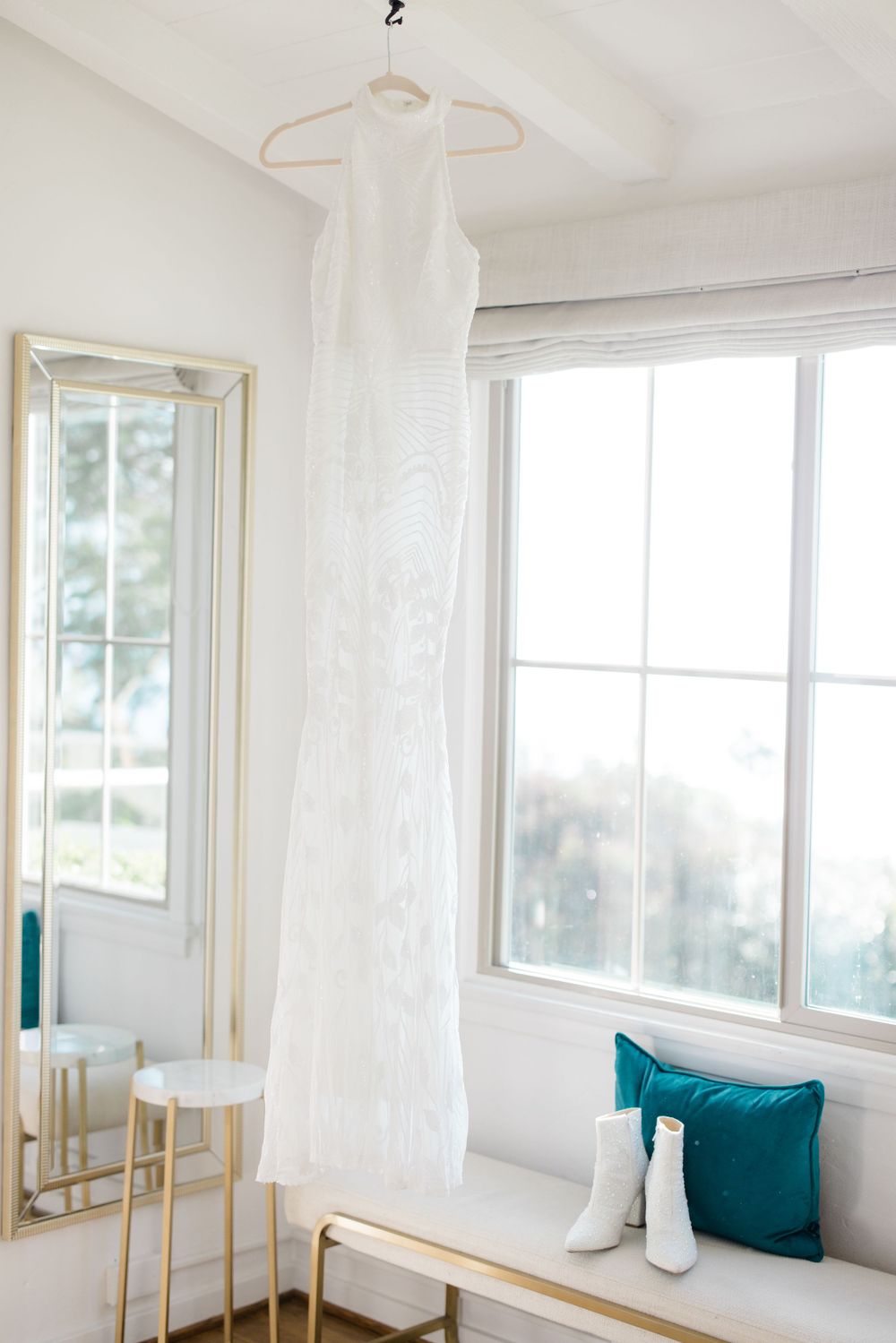 Bright white interior room with teal accent pillows and gold-framed mirrors creating an elegant coastal atmosphere.