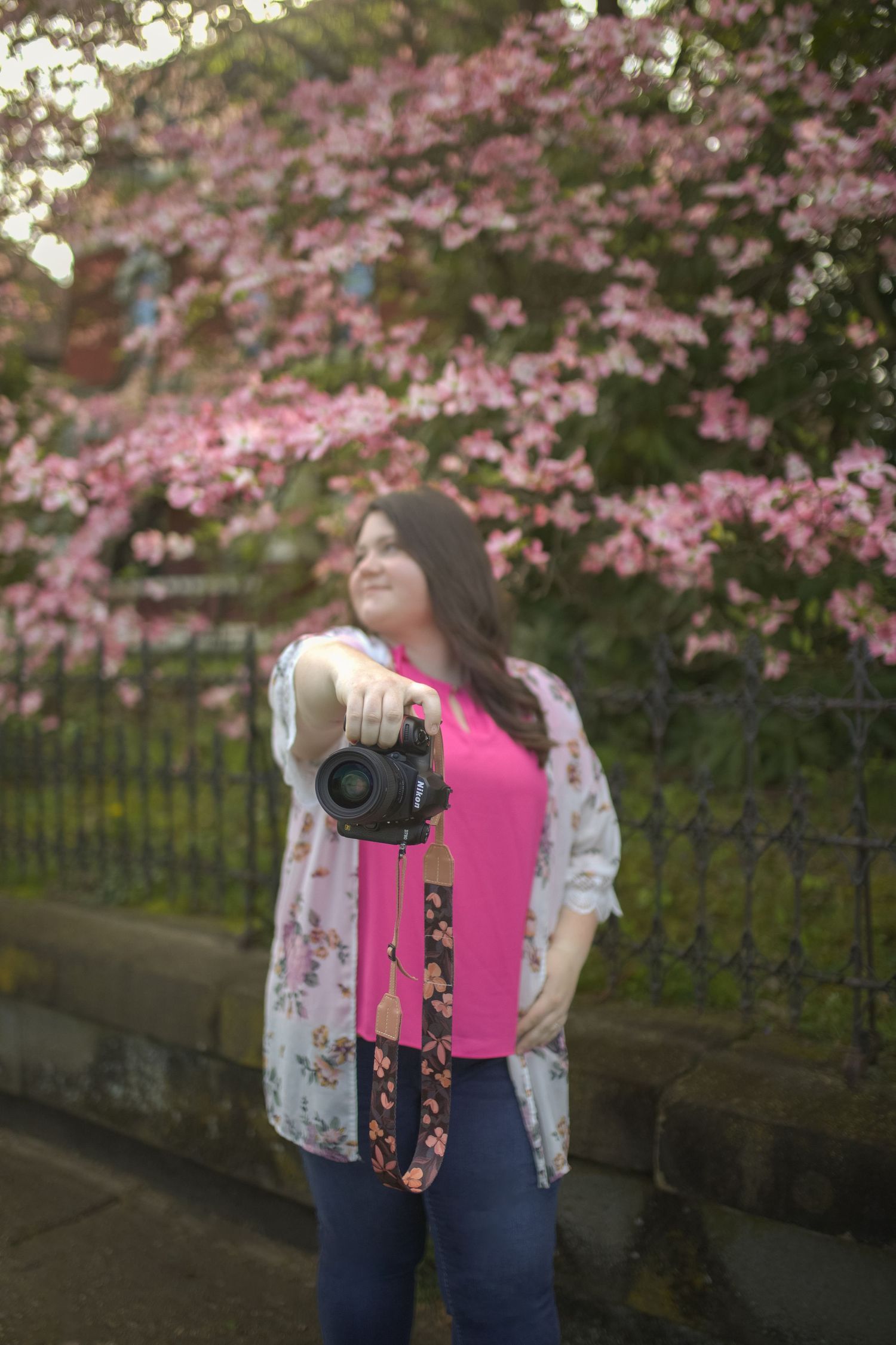 Photographer with camera poses against pink cherry blossoms in a spring garden setting.