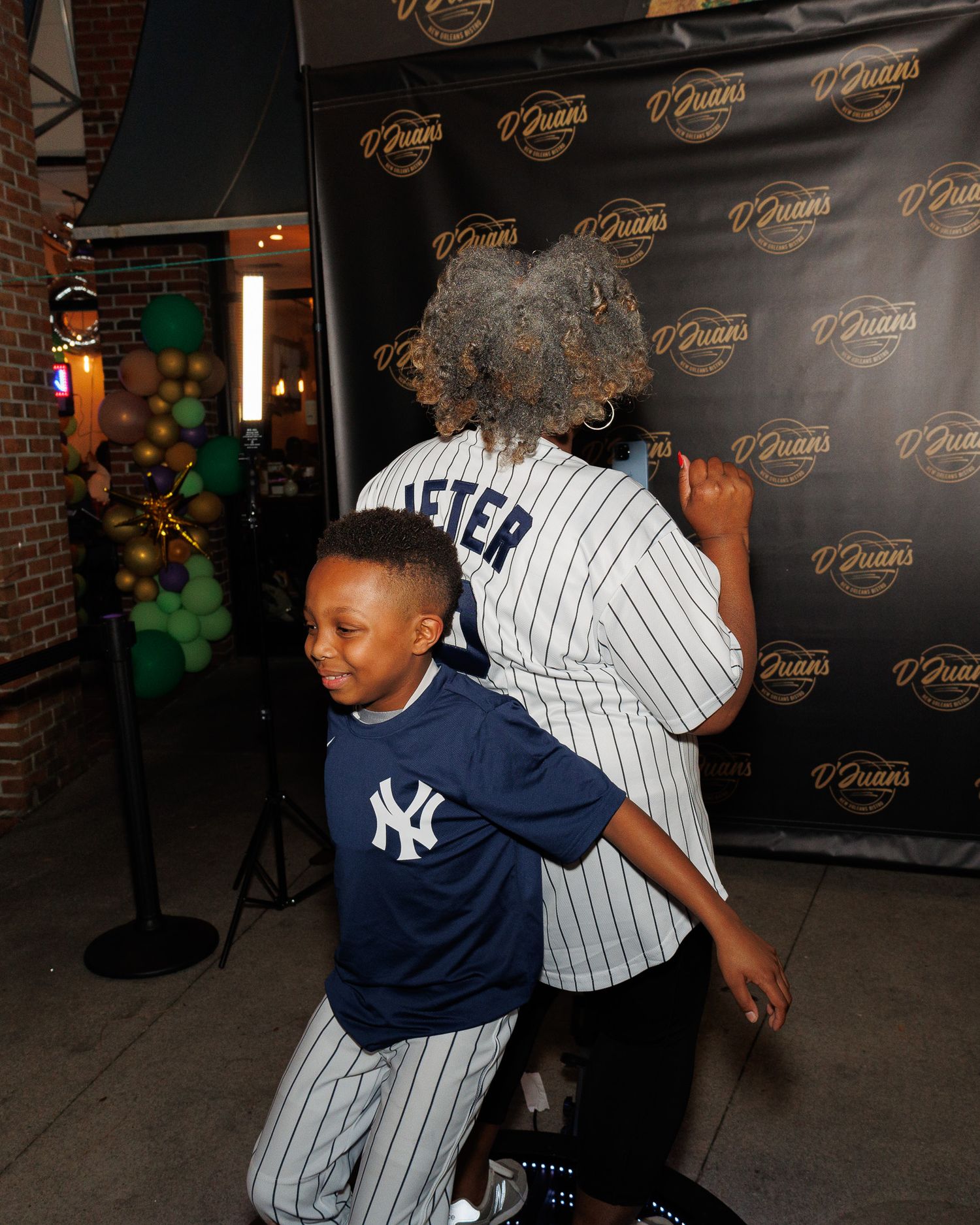 People in Yankees attire dance and pose energetically in front of a branded backdrop.