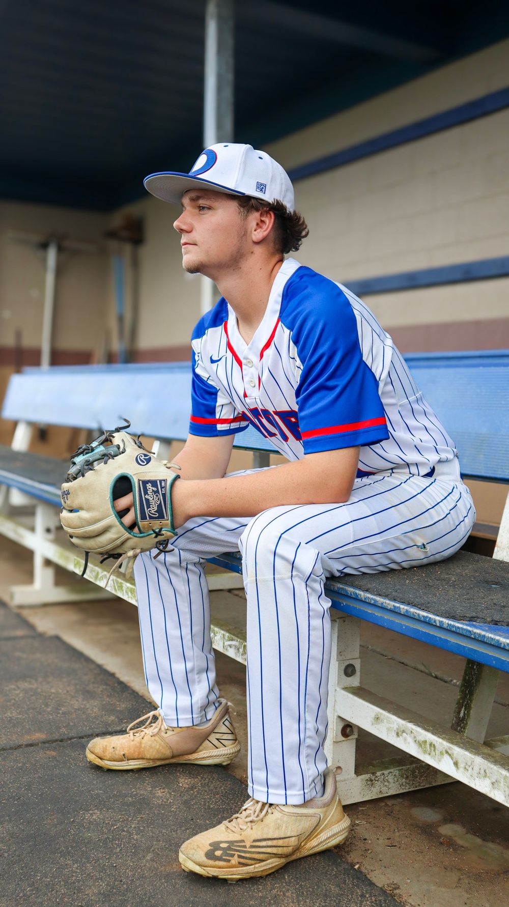 Baseball player in pinstriped uniform sits contemplatively in dugout.