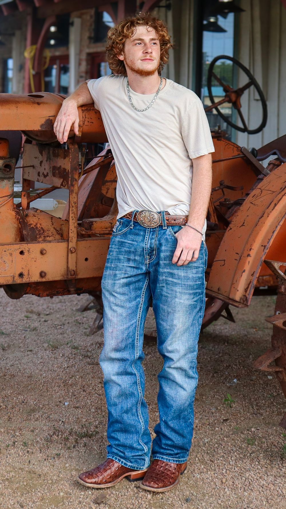 Person posing against vintage orange tractor in casual denim and t-shirt outfit.