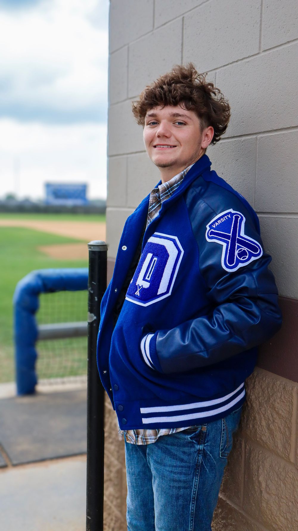 Athletic varsity letterman jacket pose by sports field with blue and white school colors.