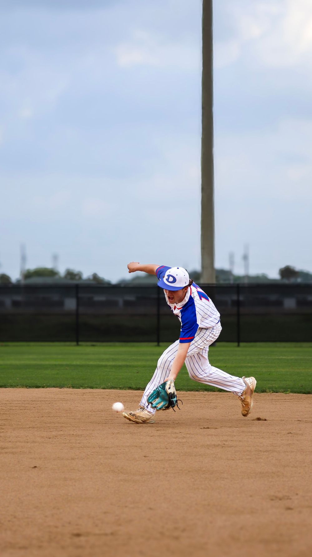 Baseball player in pinstriped uniform demonstrates fielding stance on dirt infield.