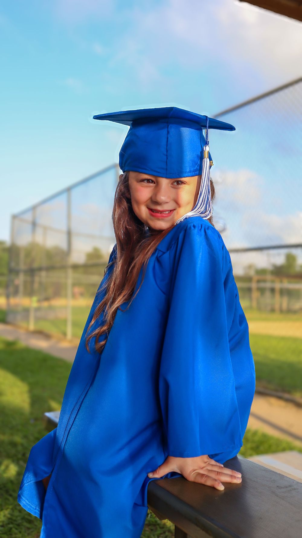 Graduate in bright blue cap and gown poses outdoors on a sunny day.