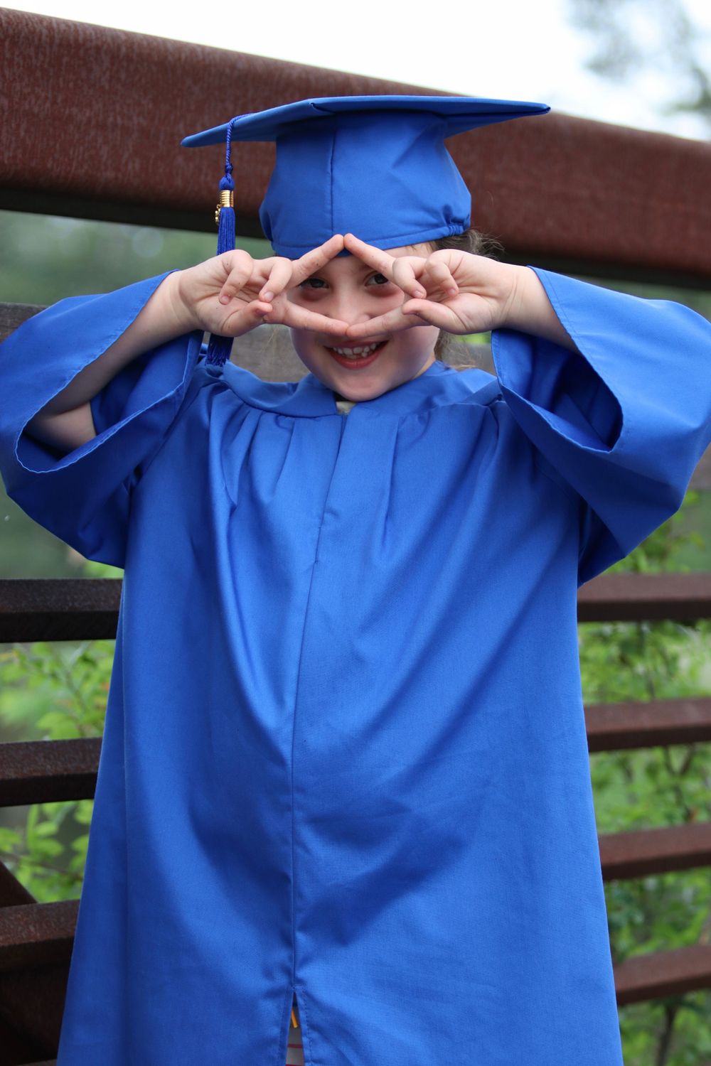 Series of playful poses in a bright blue graduation gown on a wooden bridge.