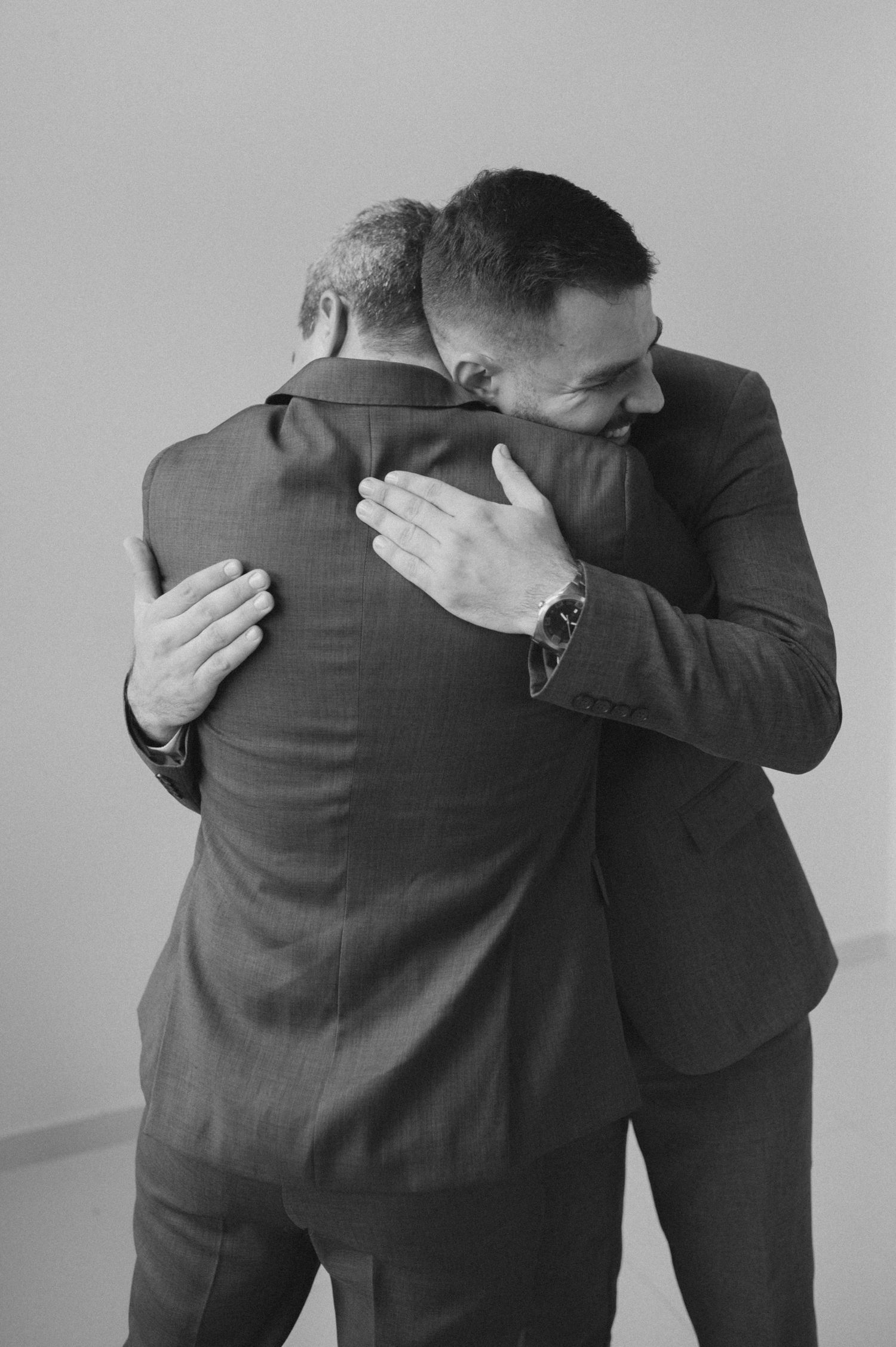 Two men in suits share an emotional embrace in black and white photography.