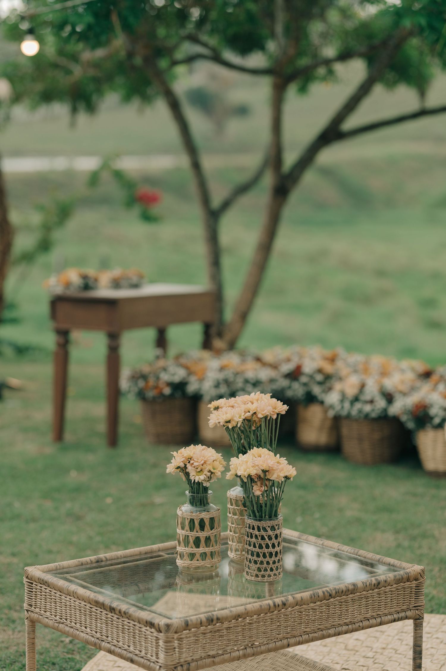 Rustic wedding decor with floral arrangements on wicker table in garden setting.