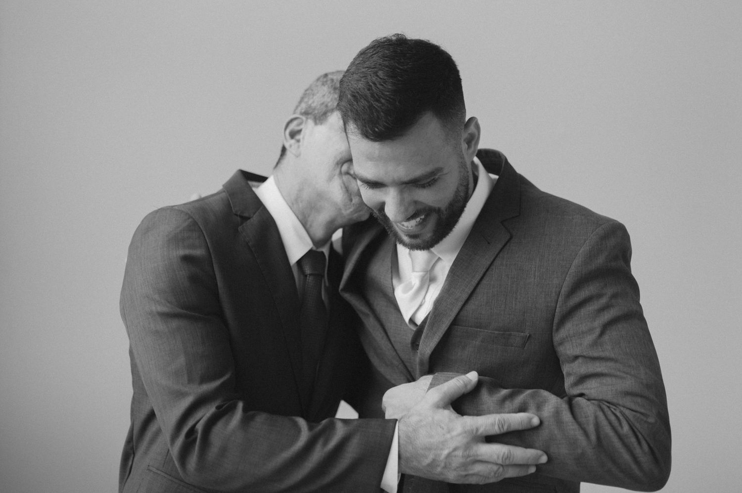 Black and white candid moment of two men in suits sharing laughter.