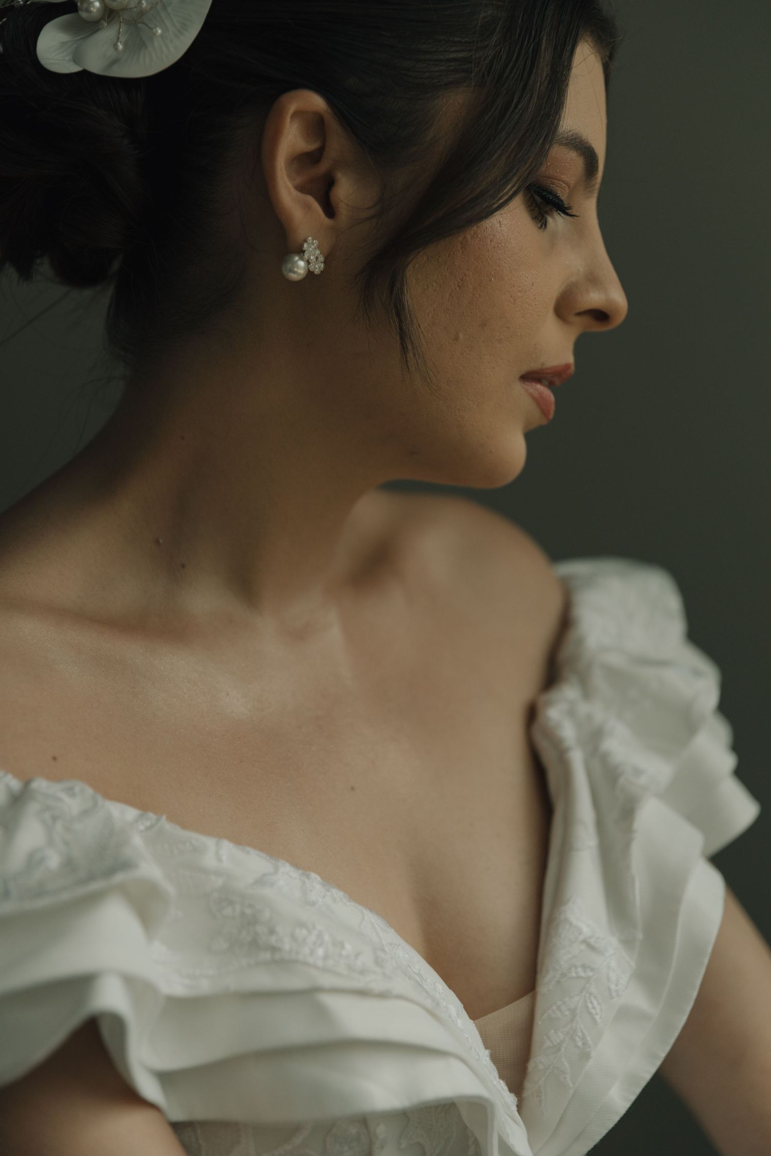 Side profile portrait showing delicate bridal makeup and floral hair accessory.