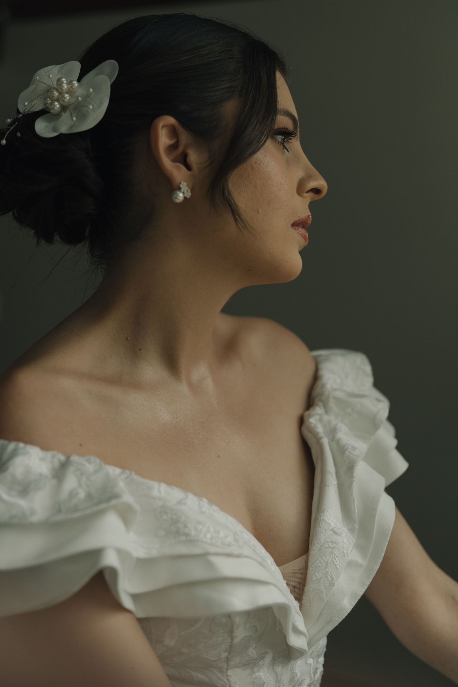 Elegant side profile portrait in off-shoulder wedding dress with orchid hair accessory.
