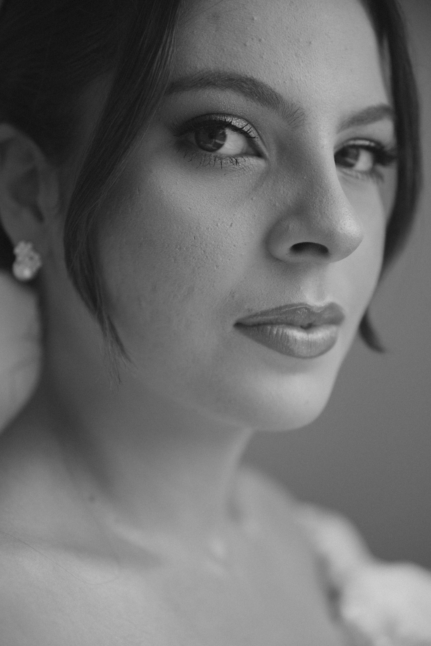 Close-up black and white portrait showing classic bridal makeup and pearl earrings.