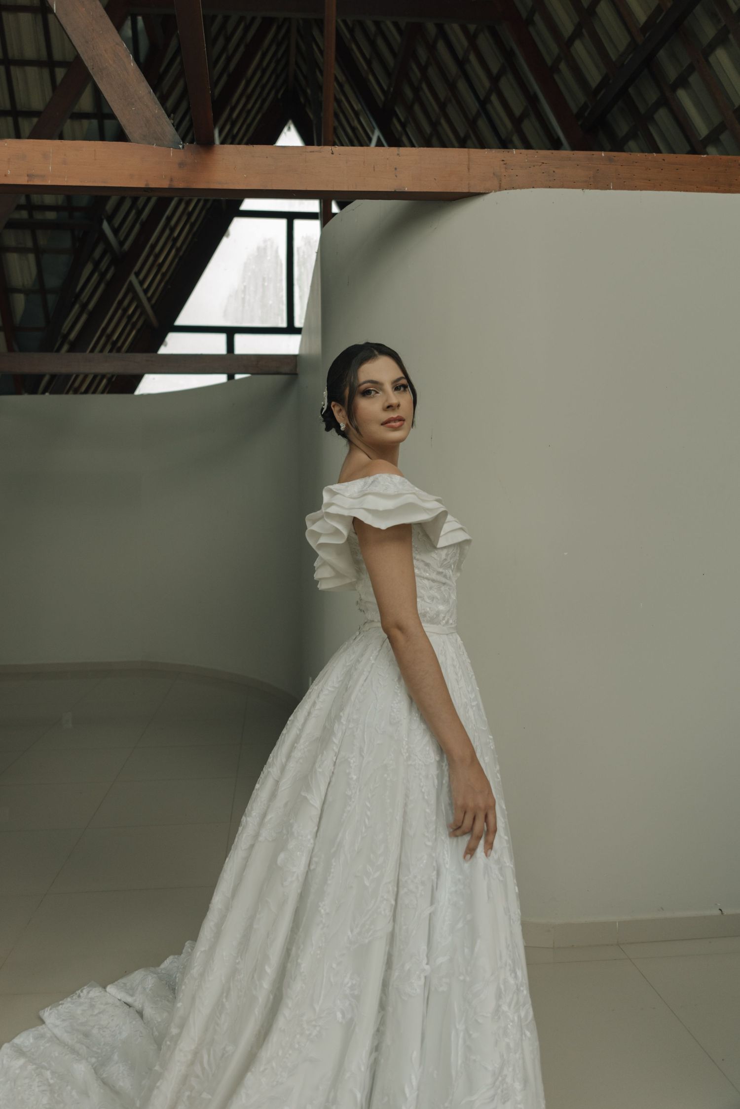 Full-length portrait of bride in classic white ball gown under rustic beamed ceiling.