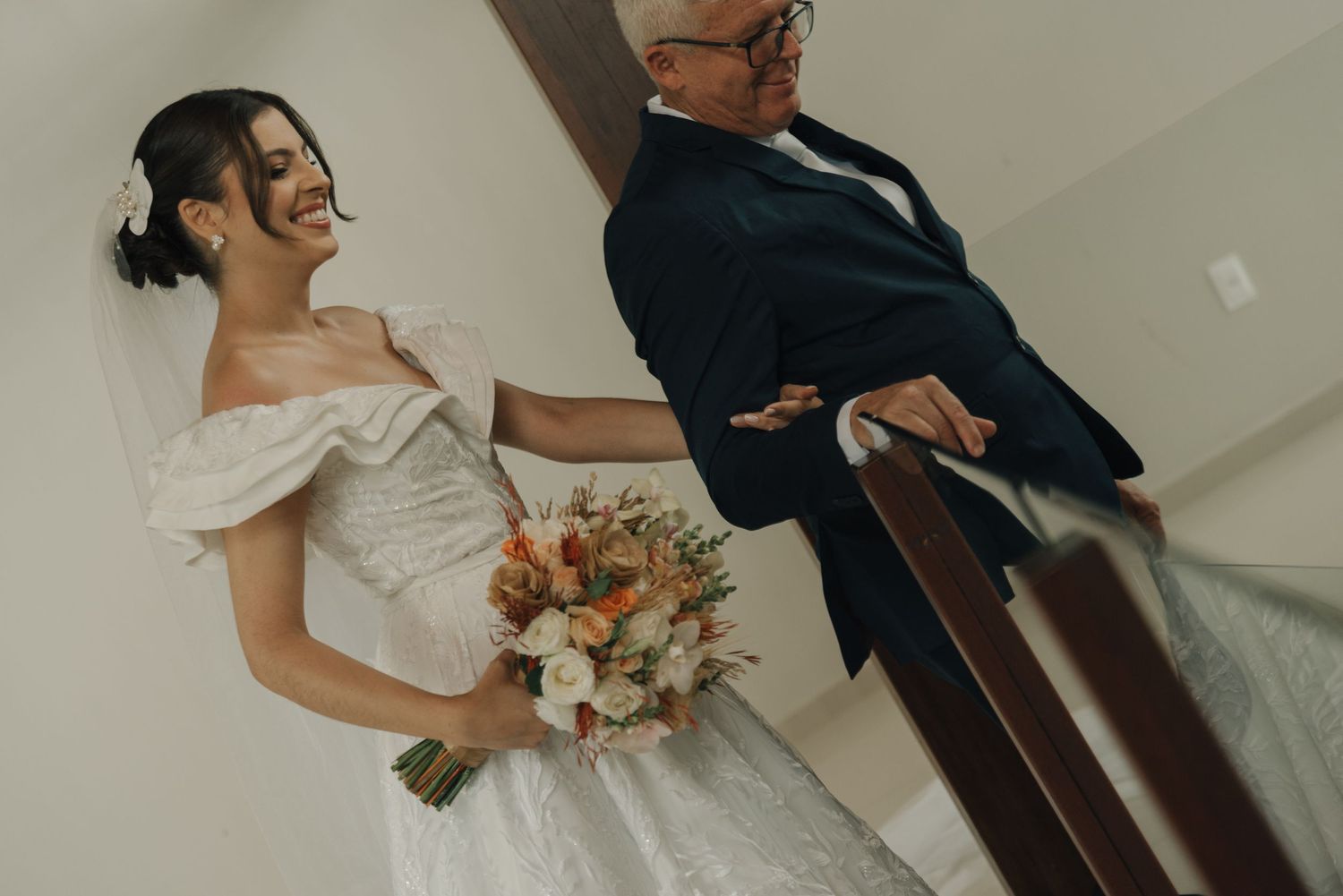 A bride in a white ball gown stands with someone in a navy suit holding flowers.