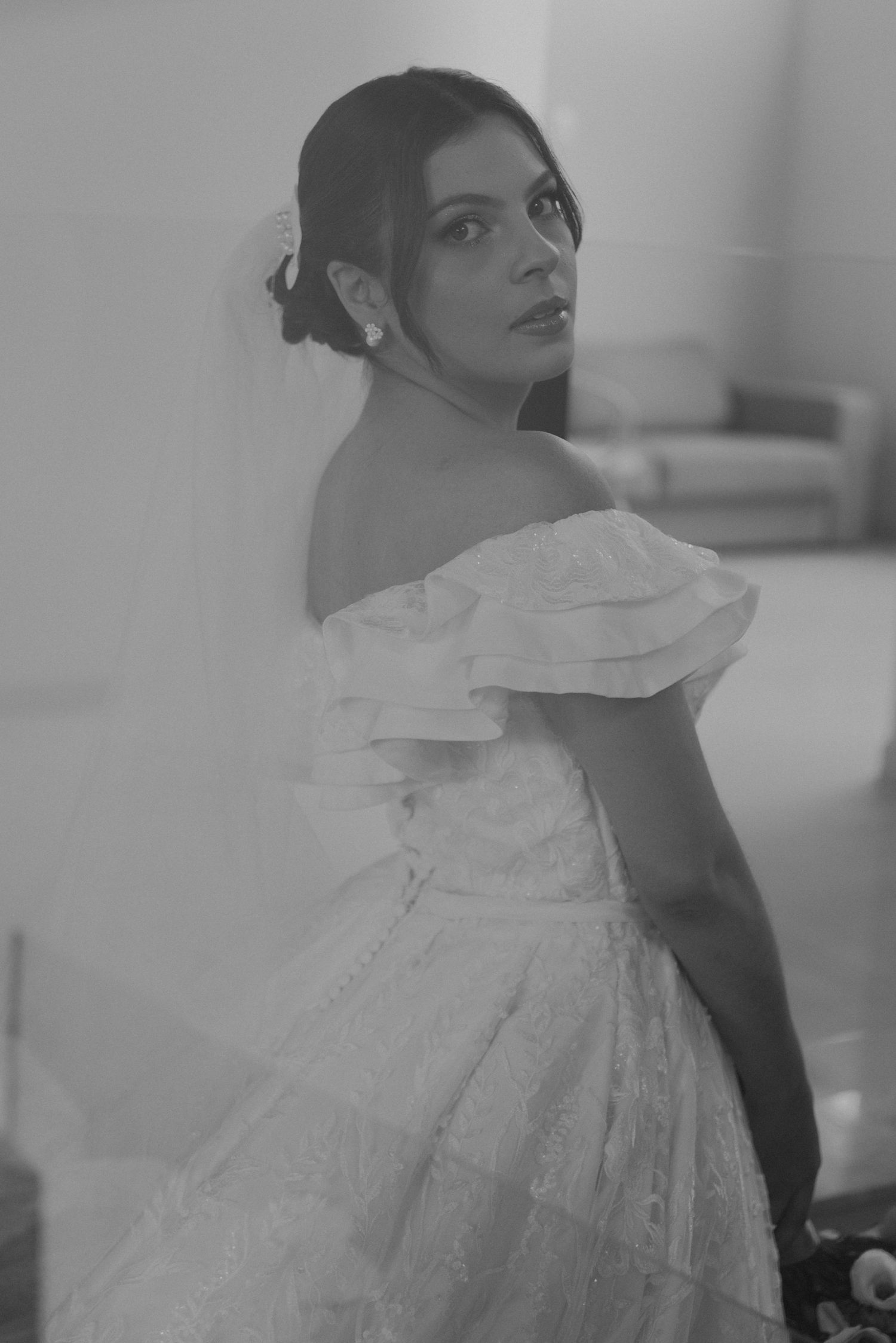 Black and white portrait of a bride in an off-shoulder wedding dress looking over her shoulder.