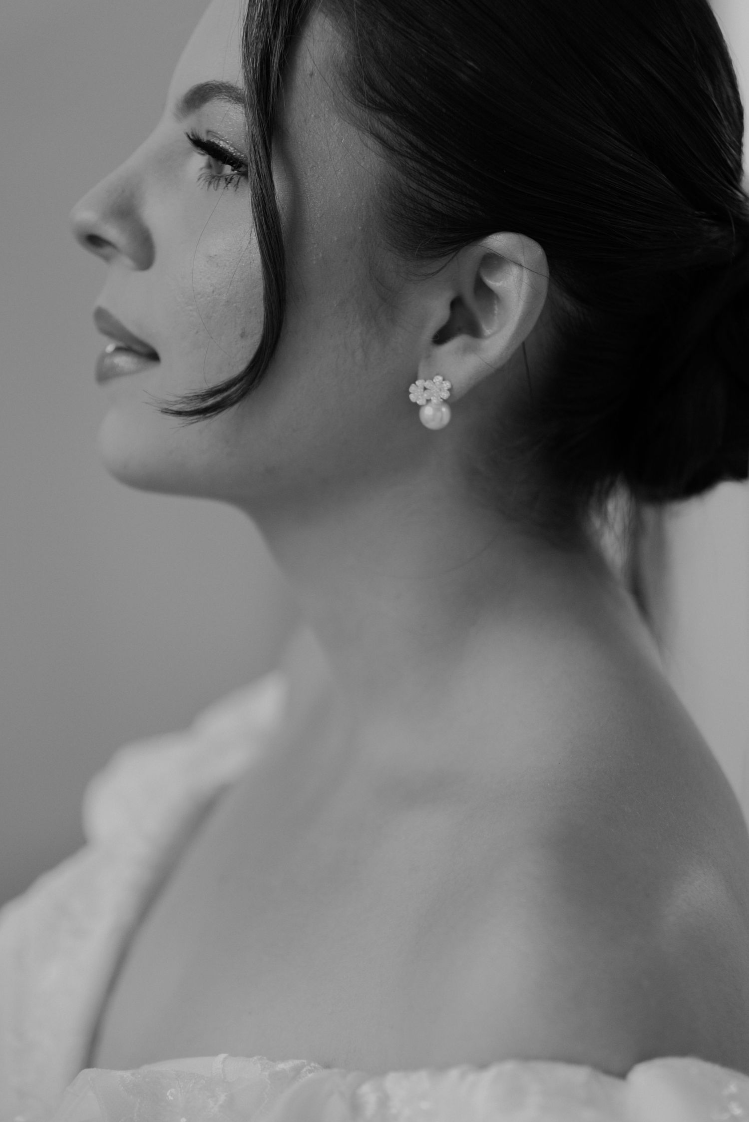 Profile view of a bride with elegant updo and floral earrings in black and white.