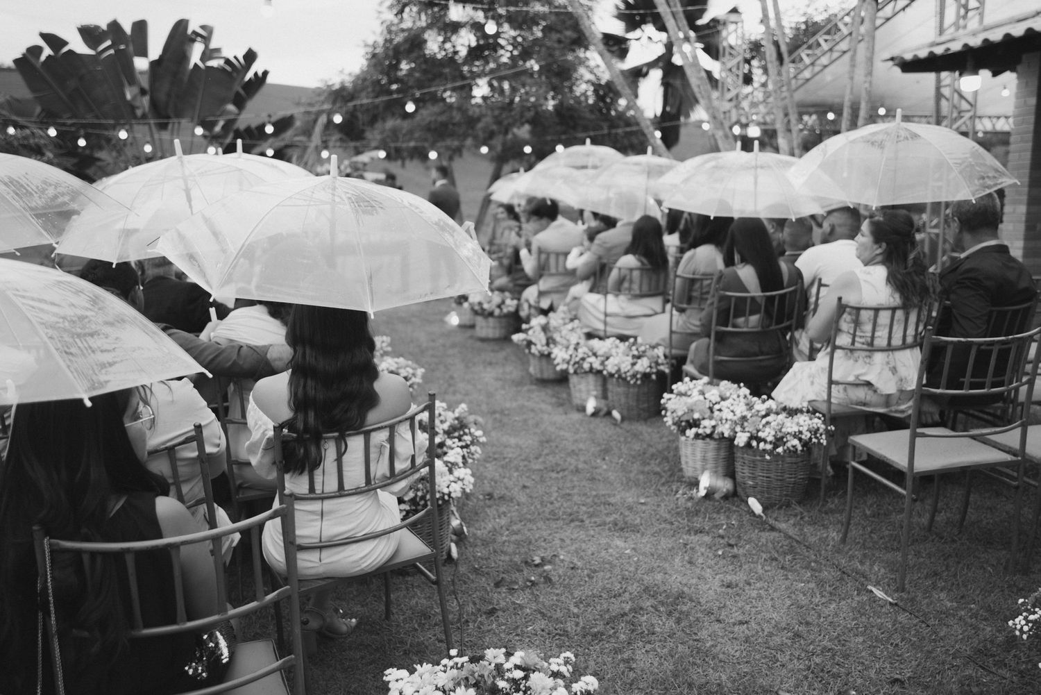 Vintage black and white photo of wedding guests with umbrellas seated in garden rows.