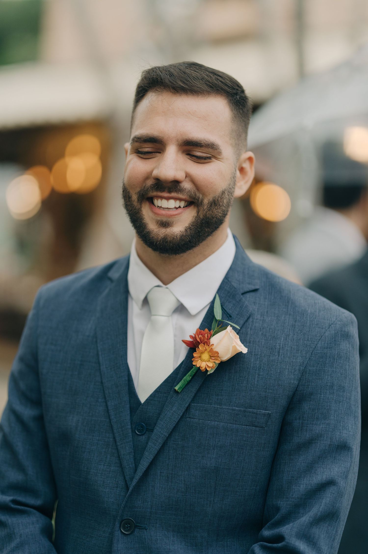 Portrait of groom in navy suit with boutonniere smiling outdoors.