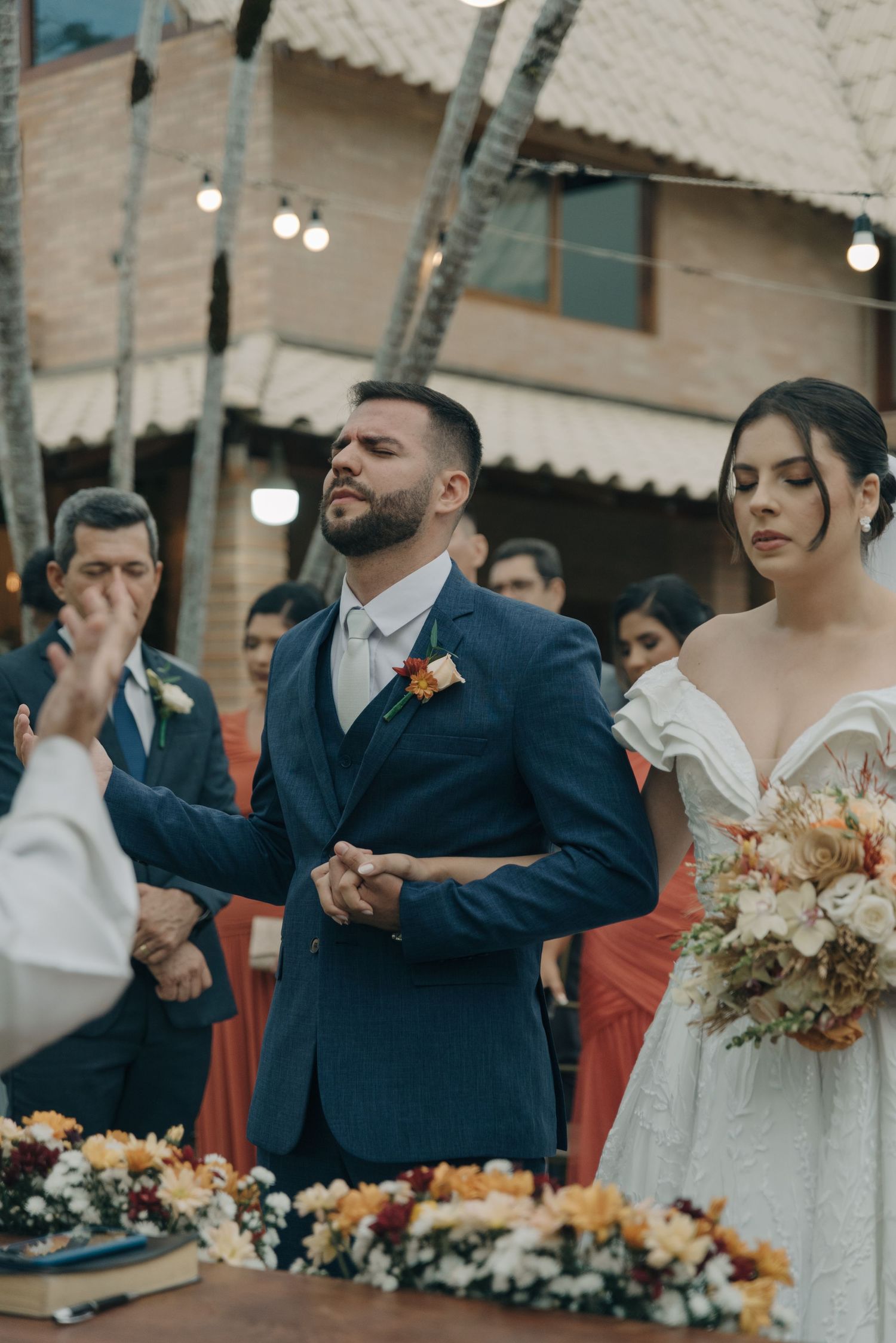 A wedding ceremony moment showing deep emotion with decorative lights and flowers in the background.