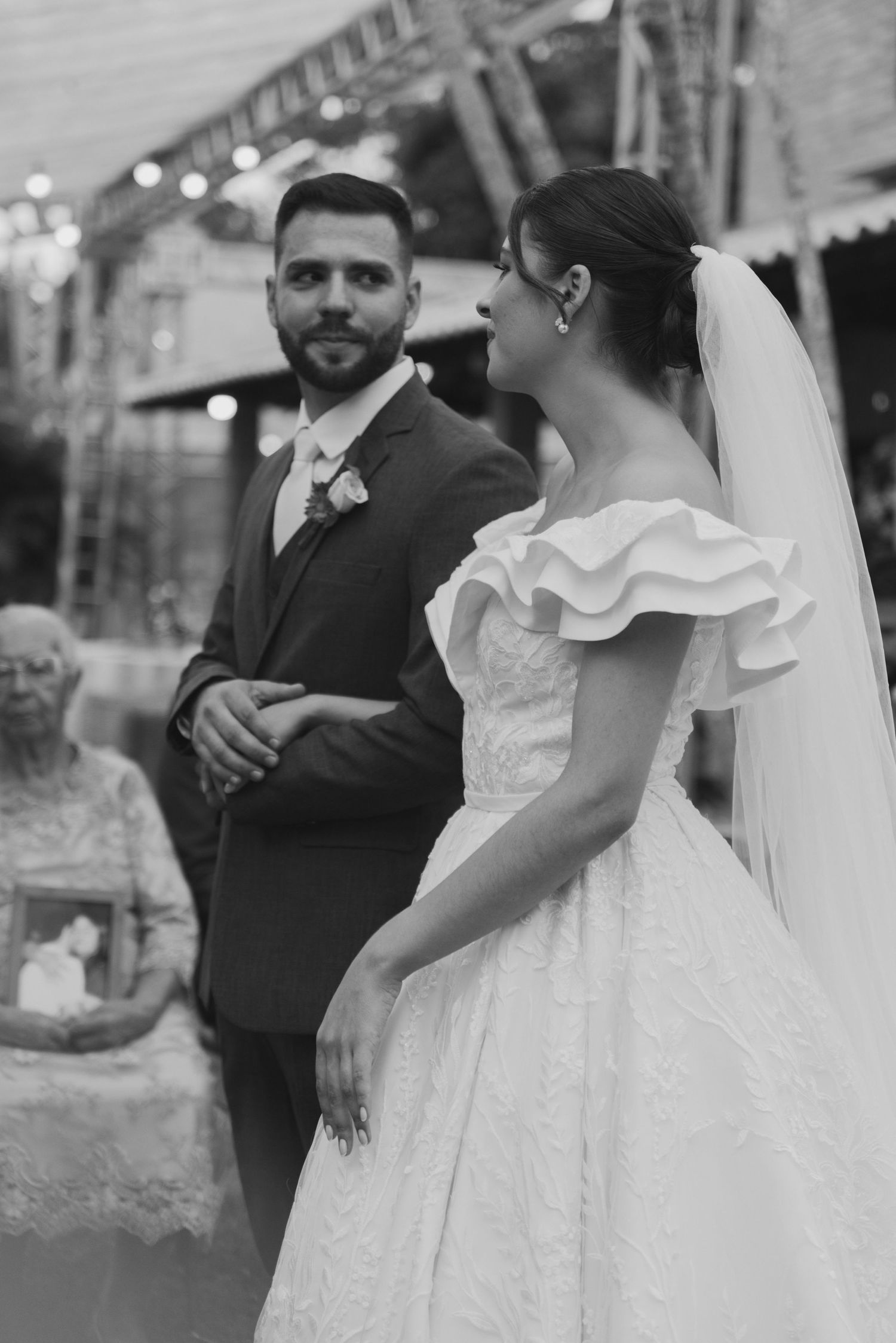 A black and white wedding portrait showing a tender moment under decorative lighting.