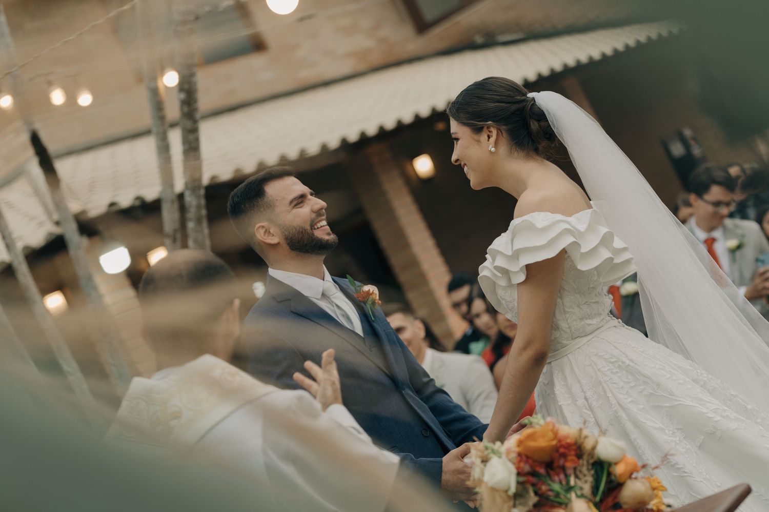 Joyful wedding moment captured with a bride in white dress and groom in navy suit exchanging glances under ambient lighting.
